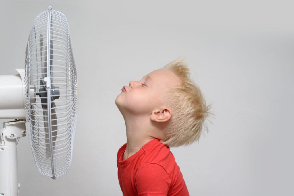Little boy standing in front of fan trying to cool off from Texas summer heat