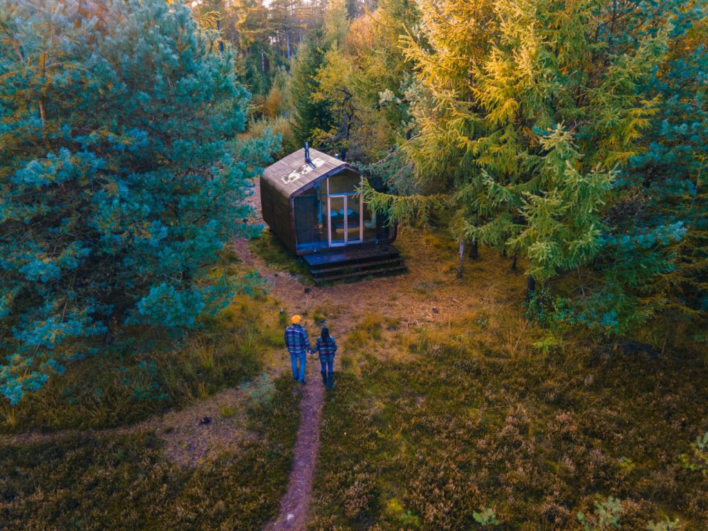 How urban families can live off the grid. Photo of couple walking toward their tiny cabin in the woods.
