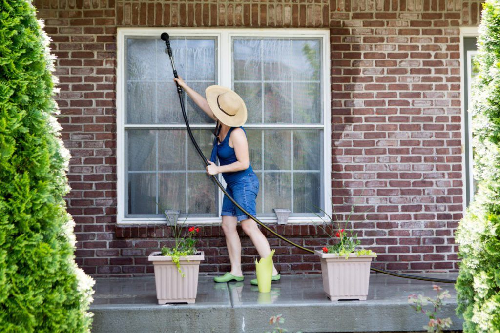 Spring cleaning maintenance tips to get your house ready for the warm weather. Photo of a woman washing her windows on her porch.