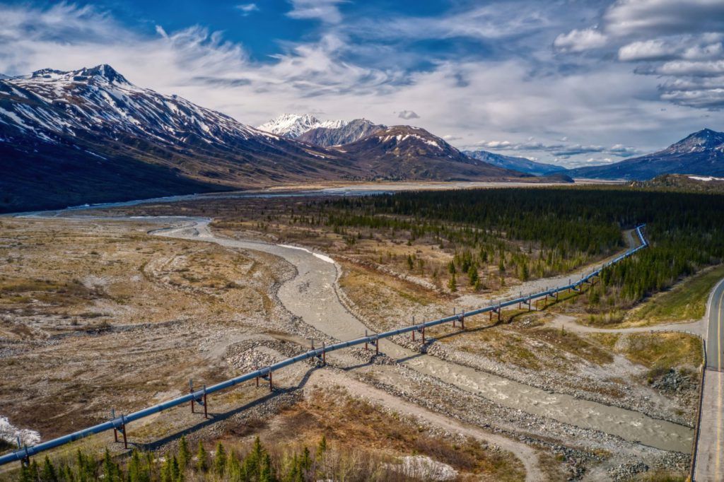 The Willow Project is sparking debate across the US as it is a controversial project impacting the environment and Alaskan residents. Photo of an oil pipeline paving through a mountain valley.