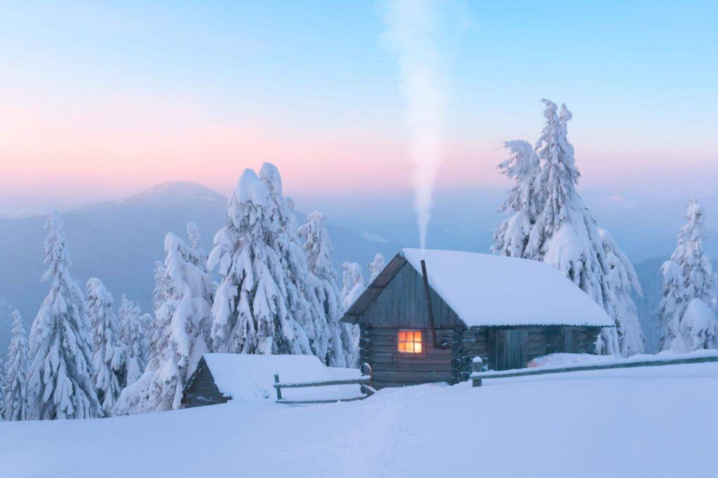 Keep you winter electricity bill down with these helpful tips. Photo of log cabin in snowy mountains.