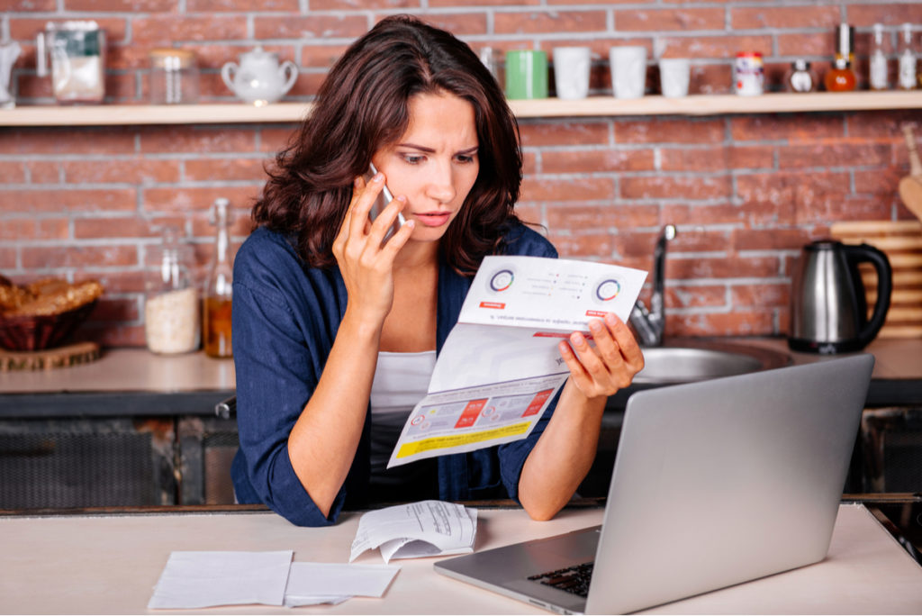 Woman looking at utility bill while on phone.