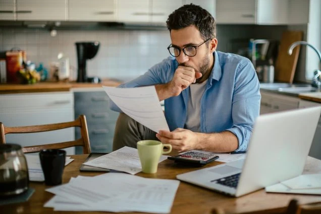 The pros and cons of budget billing. Photo of a man in his kitchen going through mail.